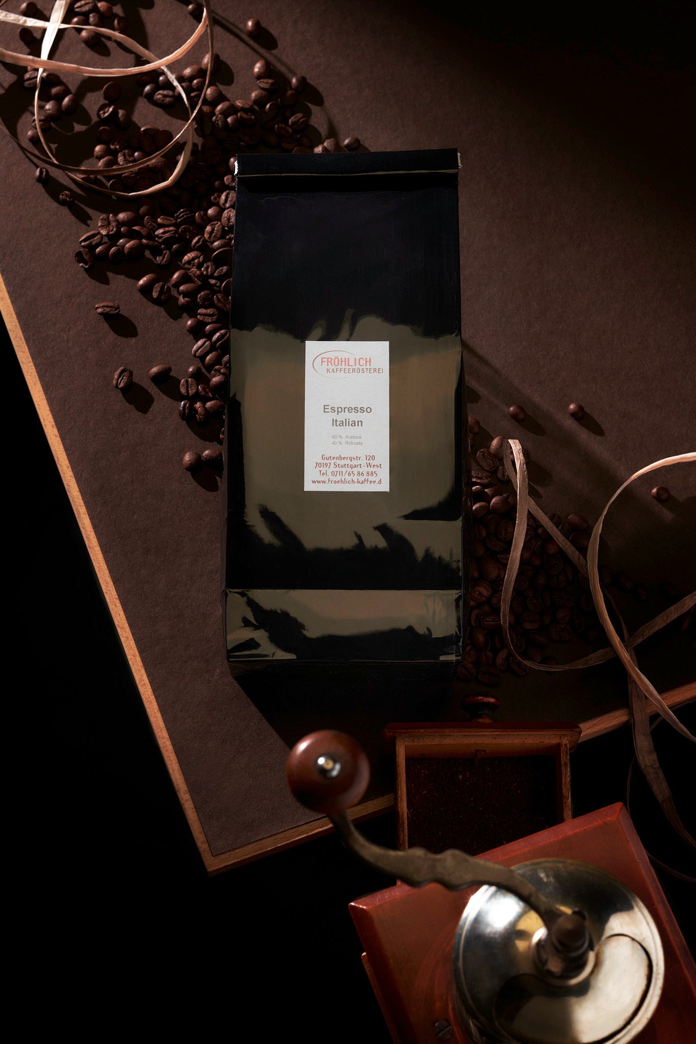 Schwarze, glänzende Kaffeetüte auf braunem Tisch mit alter Kaffeemühle und Kaffeebohnen