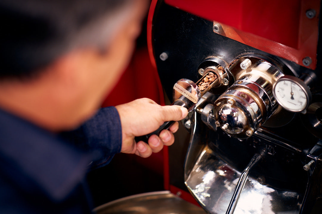 Detailfoto des Röstmeisters am Probenzieher, der mit Kaffeebohnen gefüllt ist, rote Röstmaschine