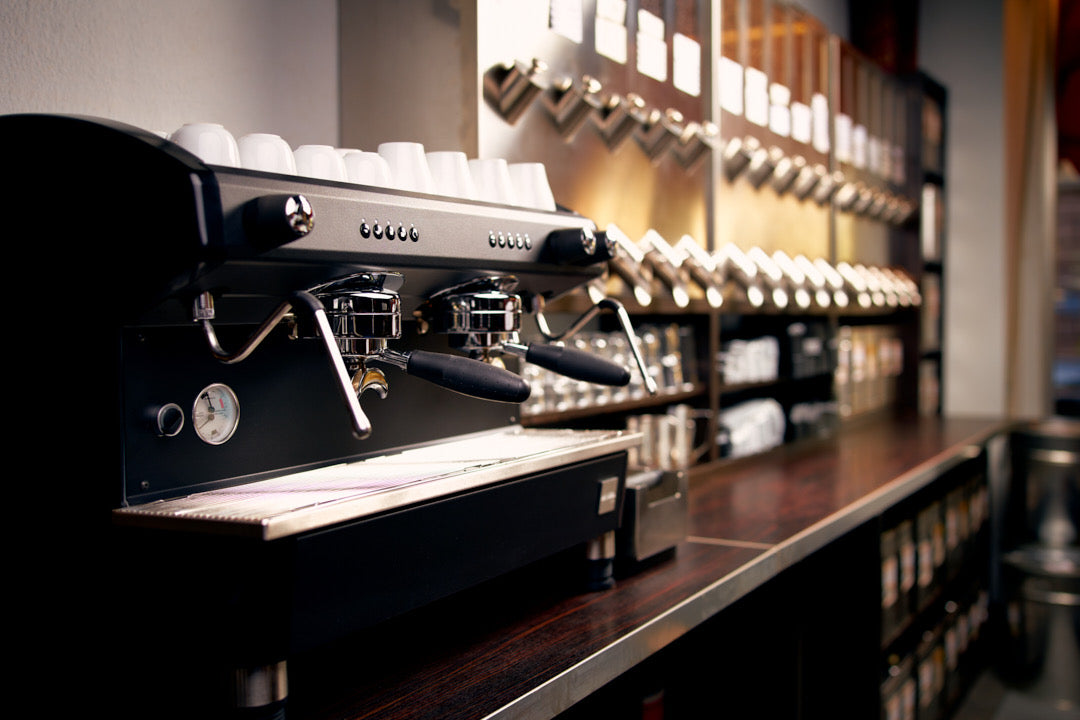 Große, schwarze Espressomaschine mit Edelstahl-Kaffeeschütten im Hintergrund